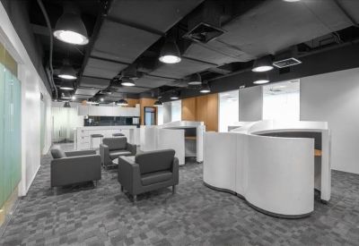 Lounge area with dark grey armchairs and curved white privacy pods under industrial ceilings.
