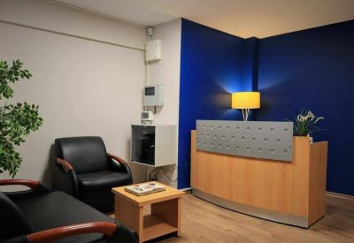 Reception area with a wooden front desk, black leather seating, and a bold blue feature wall.