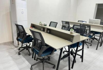 Bright open-plan workspace featuring rows of desks with blue-seated ergonomic chairs.