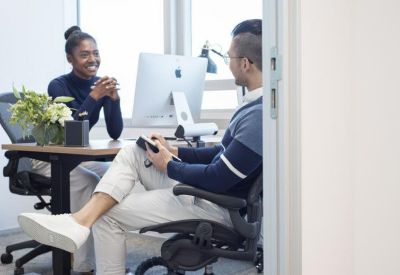 Two colleagues talking at a desk in a bright, modern office suite.