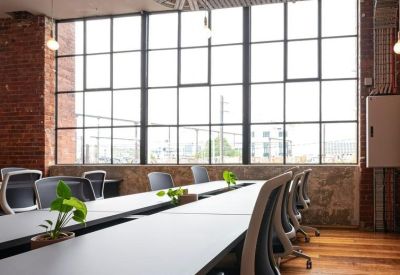 Bright open-plan office with white desks and mesh chairs against a brick wall and large windows.