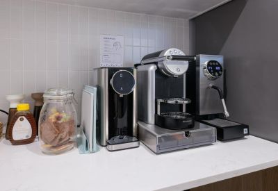 A communal kitchen countertop equipped with multiple coffee machines and a jar of snacks.