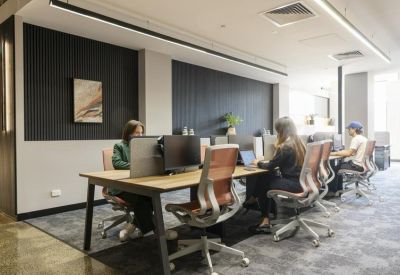 Modern open-plan workspace with wooden desks and ergonomic mesh chairs against a dark feature wall.