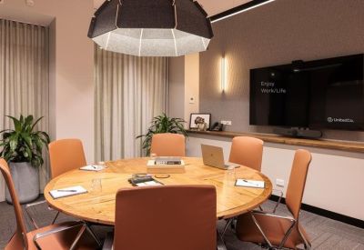 Small meeting room with a round wooden table, tan leather chairs, and a large wall-mounted screen.
