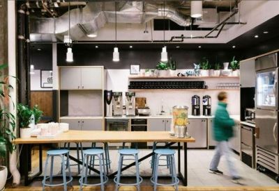 Modern office kitchen area with a large wooden island and blue bar stools.