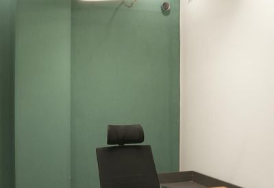 Private office with a light wood desk, teal feature wall, and modern ring pendant light.