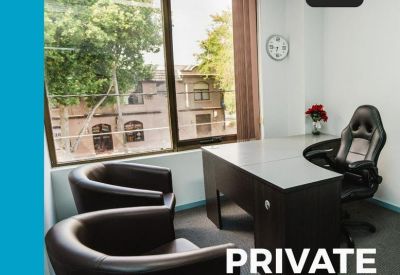 Private office suite with a large window, dark wood desk, and leather seating.
