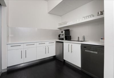 Modern white kitchenette with dark flooring and integrated appliances.