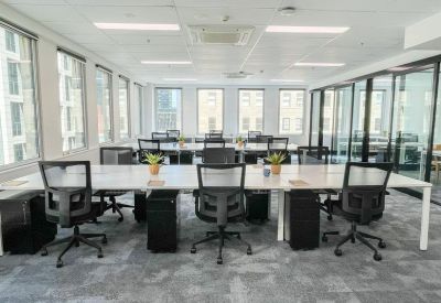 Open-plan office with rows of white desks and ergonomic black chairs near large windows.
