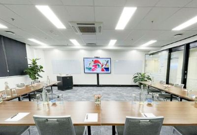 Professional boardroom with a U-shaped wooden table and large digital display screen.