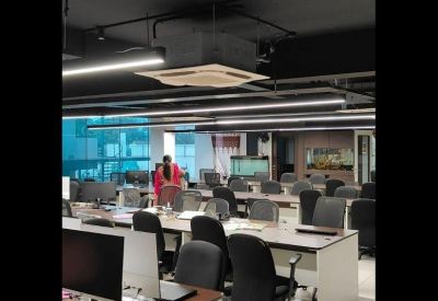 Bright coworking area with white desks, black task chairs, and a visible break area in the background.
