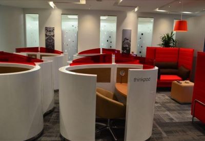 Modern communal area with curved white privacy pods, red sofas, and warm lighting.