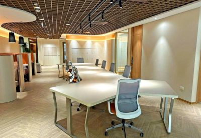 Spacious coworking area with long white desks and grey ergonomic chairs under a lattice ceiling.