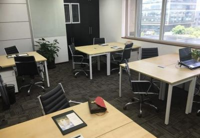 Open-plan office space with light wood desks, black chairs, and large windows.