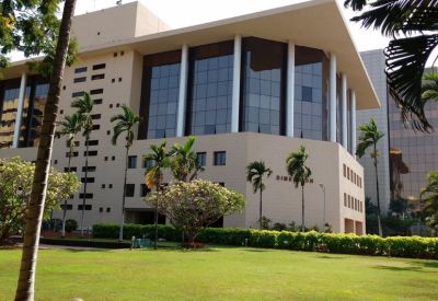 Exterior view of the 4th Dimension building featuring a glass facade and manicured green lawn with palm trees.