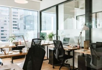 Bright glass-walled private office with ergonomic chairs and city views through large windows.
