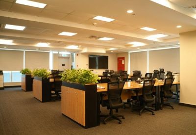 Spacious open-plan workspace featuring long wooden desks and indoor planters.