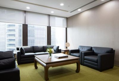 Lounge area with black leather sofas and a large wooden coffee table on a green carpet.