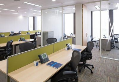 Open-plan office with rows of wooden desks, ergonomic chairs, and green privacy partitions.