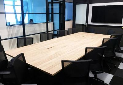 Professional boardroom with a light wood table, black mesh chairs, and a large wall-mounted screen.