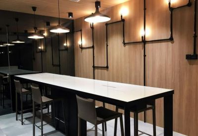 Modern long white high-top table with industrial pipe lighting on a wood-paneled wall.