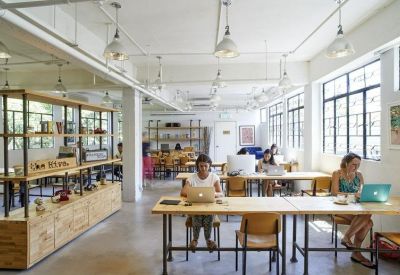 Spacious open-plan coworking area with long wooden tables and natural light.
