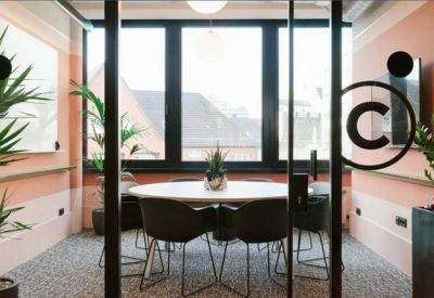 Bright glass-walled meeting room with a round table and views of the surrounding city architecture.