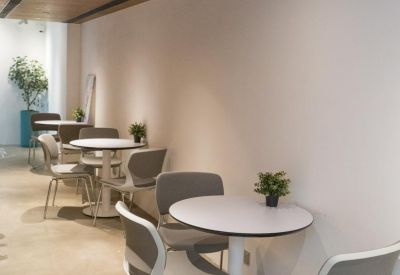 Sleek seating area with small round tables and grey chairs along a white wall.
