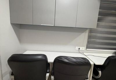 Two-person workstation under grey overhead storage cabinets with black leather chairs.