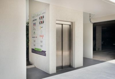 Building entrance featuring a silver elevator and a directory sign on the white wall.