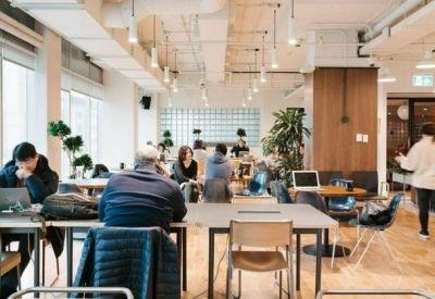 Bright open-plan workspace with long tables, ergonomic chairs, and large windows.