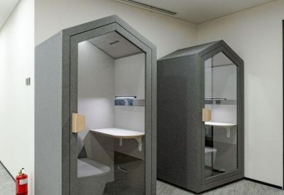 Two house-shaped acoustic phone booths in a grey and white hallway.