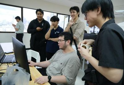 A group of colleagues collaborating around a computer screen in a bright, shared workspace.