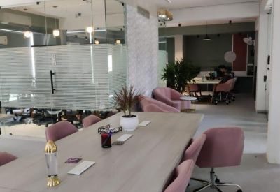 Large wooden communal table with pink velvet chairs and green plants.