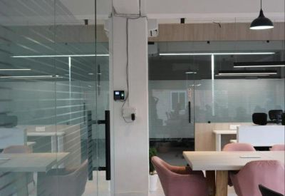 View of a modern office hallway with glass walls and pink chairs in the background.