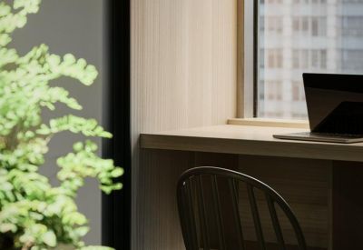 Close-up of a fern plant in a glass terrarium next to a wooden desk and chair.