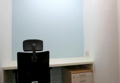 Compact private office suite with a black ergonomic chair and light blue accent wall.