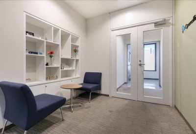 Small waiting area with blue armchairs, a round side table, and white shelving unit.