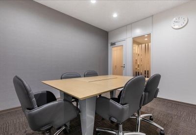 Modern conference room with a light wood table, grey chairs, and a wall clock.