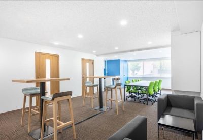 Communal breakout area with high tables, wooden stools, and green accent chairs.