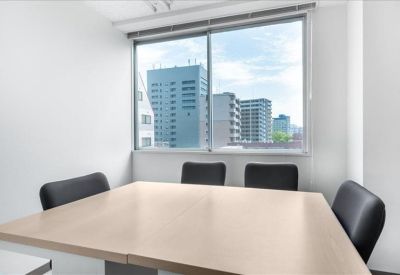 Sunlit meeting room with a light wood table and four black chairs near a large window.