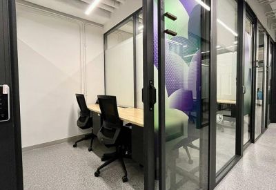 Private glass-walled office suite with two black ergonomic chairs and a light wood desk.