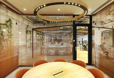 Bright glass-walled office space with a round wooden table and orange chairs.