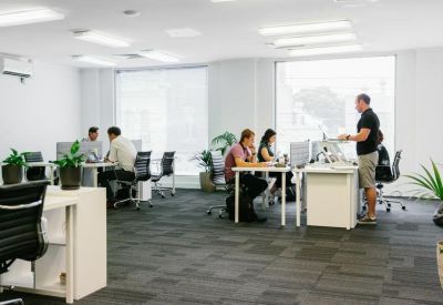 Open-plan coworking area with natural light and people working at white desks.