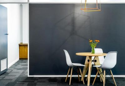 Round meeting table in front of a dark chalkboard wall with modern white chairs.