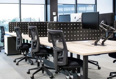 Open-plan workspace with light wood desks, ergonomic chairs, and privacy screens.