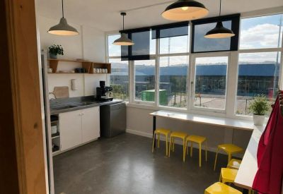 Bright communal kitchen and dining area with yellow stools and industrial pendant lighting.