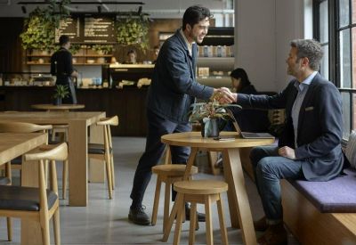 People networking in a bright communal cafe area with wooden furniture and a barista counter.