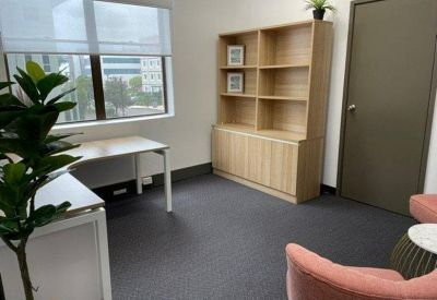 Private office suite with a wooden bookshelf, potted plant, and pink velvet armchairs.