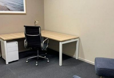 Internal office with an L-shaped desk, ergonomic chair, and coastal wall art.